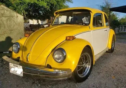 Yellow and white classic Volkswagen Beetle parked outdoors in a sunny setting with Texas license plate