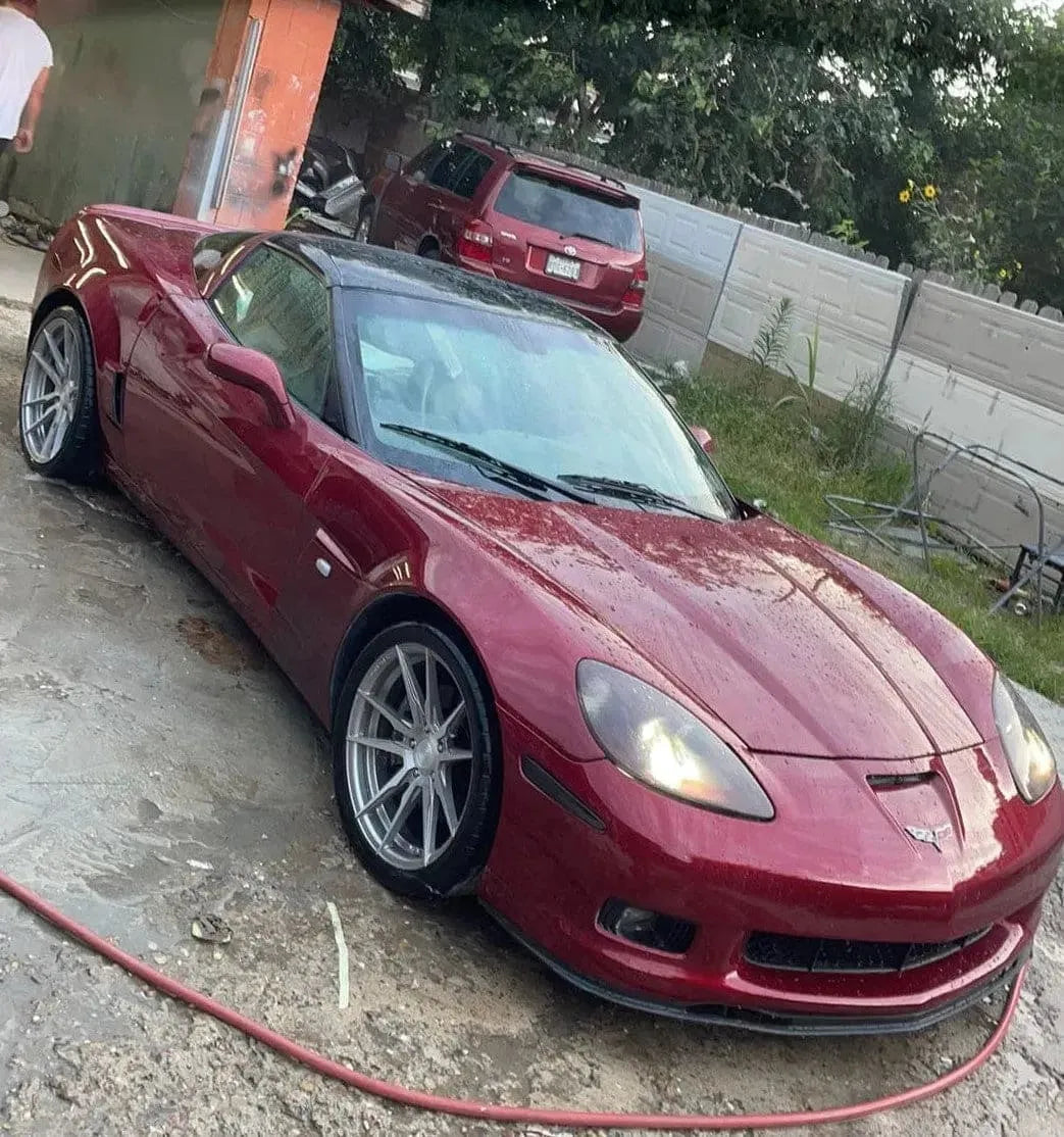 Red Chevrolet Corvette sports car parked on wet concrete near a red SUV and white fence