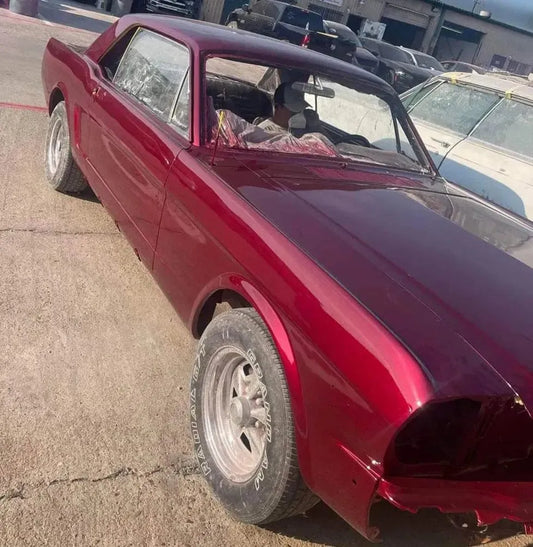Partially restored red classic car in outdoor auto repair lot with missing front light and worn tires