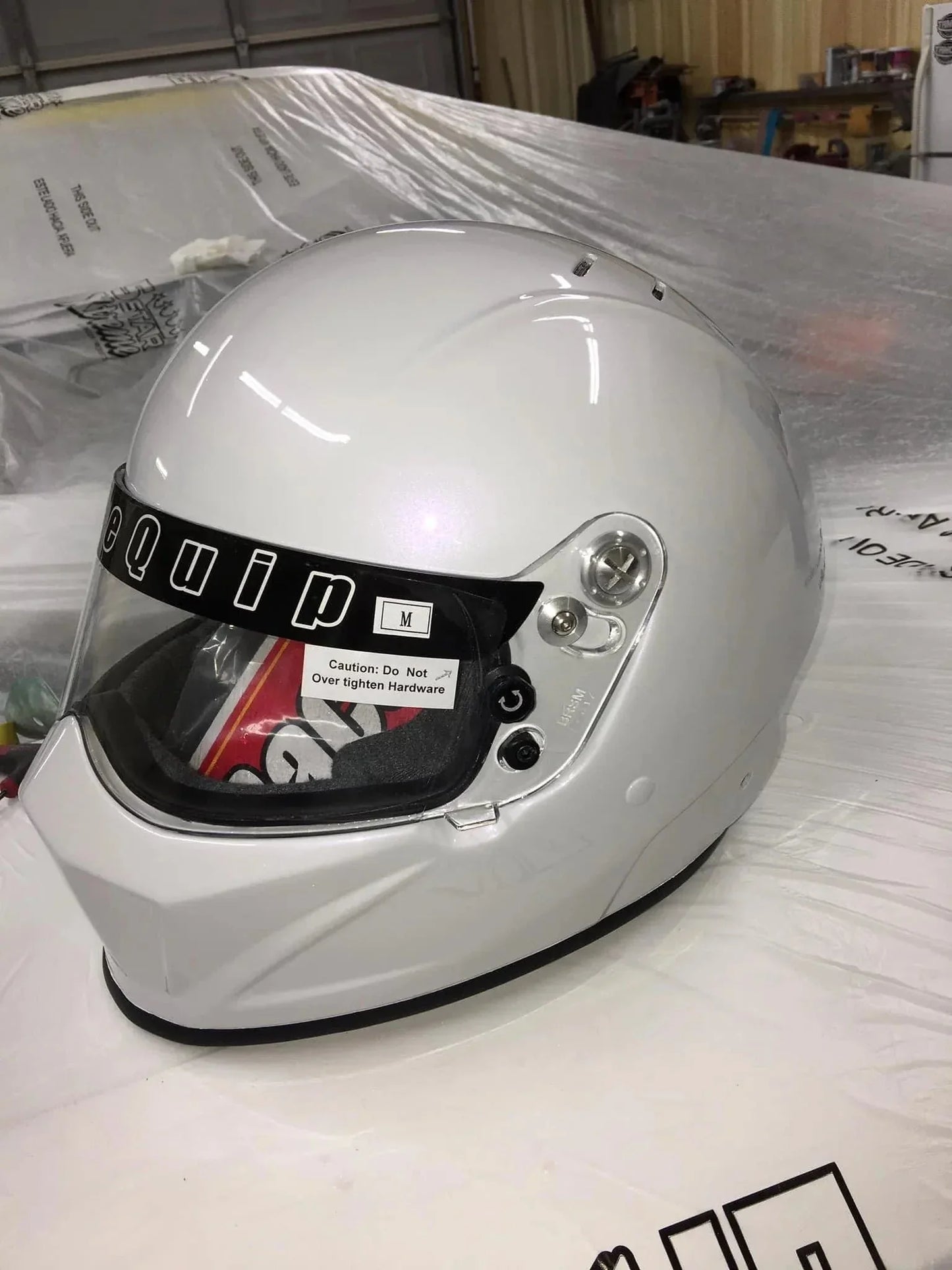 white full-face racing helmet with black visor strip reading 'Equipment' placed on plastic-covered table