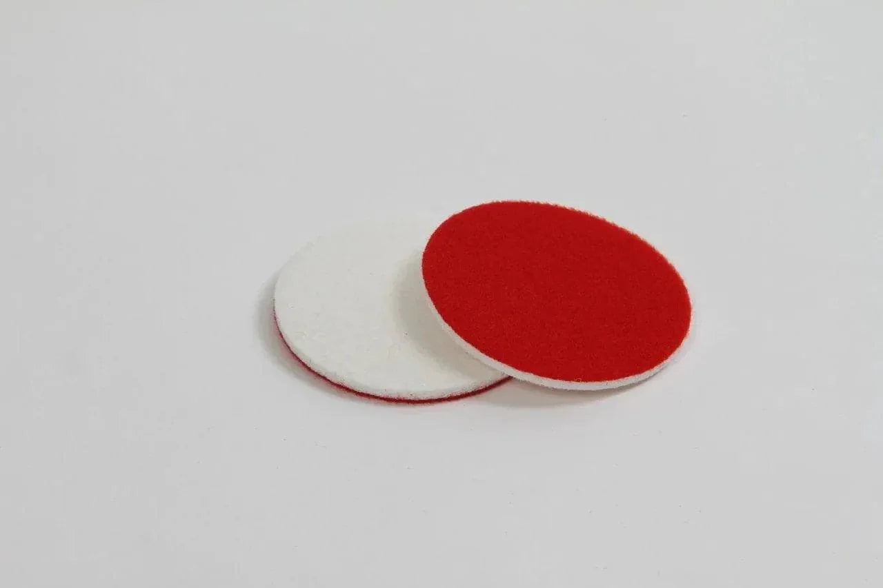 Two CarPro glass rayon polishing pads, one red side up and one white side up, on a white background