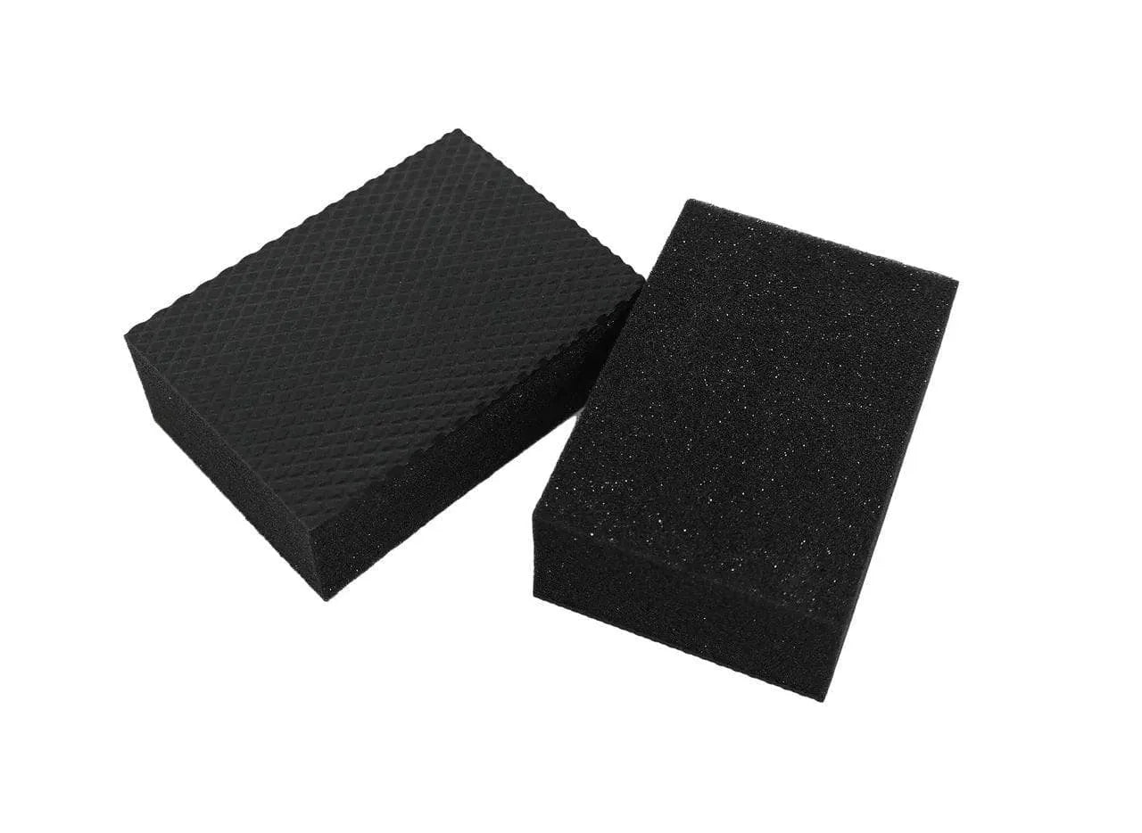 Two black CarPro Polyshave Decon Block Mini detailing sponges with textured and smooth surfaces