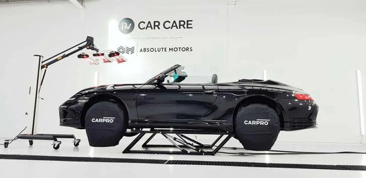 Black convertible car elevated on a lift with CarPro wheel covers in a clean car care workshop