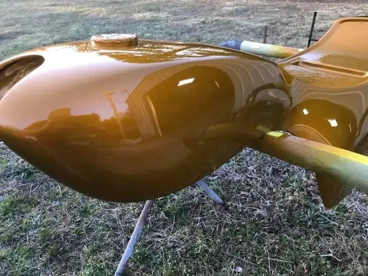 Glossy gold-painted aircraft fuselage section resting on grass outdoors with reflections of surrounding structures