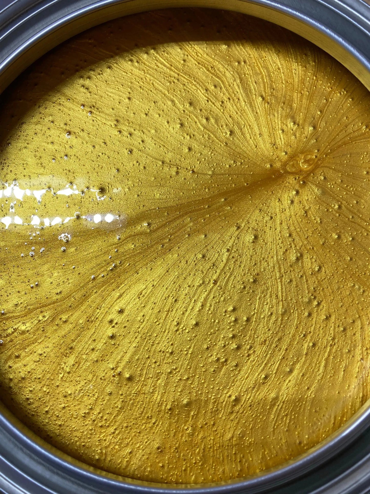 Open can of metallic gold paint with textured surface and light reflections