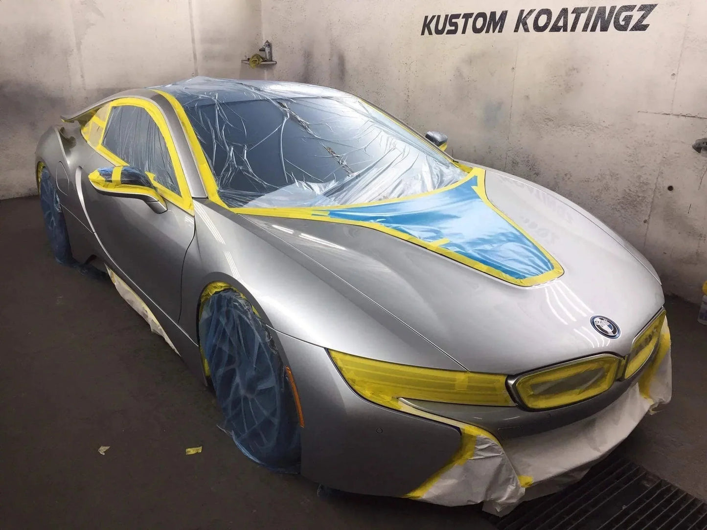 Silver BMW i8 sports car masked for automotive spray painting, with protective film and tape in a paint booth