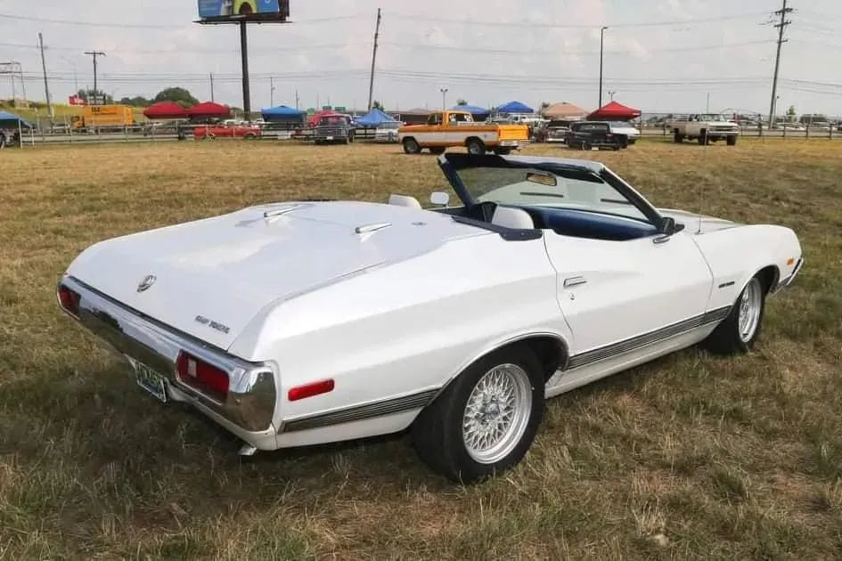 White 1970s convertible classic car parked on grassy field at outdoor vintage car event