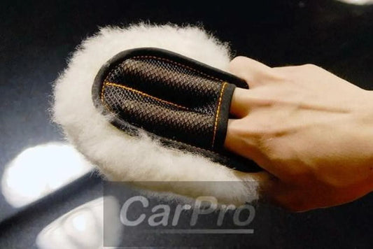 Hand wearing black two-finger mini mitt with fluffy white Merino wool for car detailing on black glossy surface