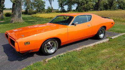 Bright orange classic muscle car parked on driveway with green grass and trees background